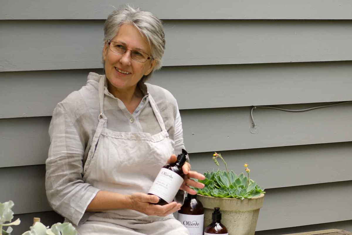 Jude sitting outside the St Andrews Beach home studio holding an Olieve & Olie Hand & Body Wash.