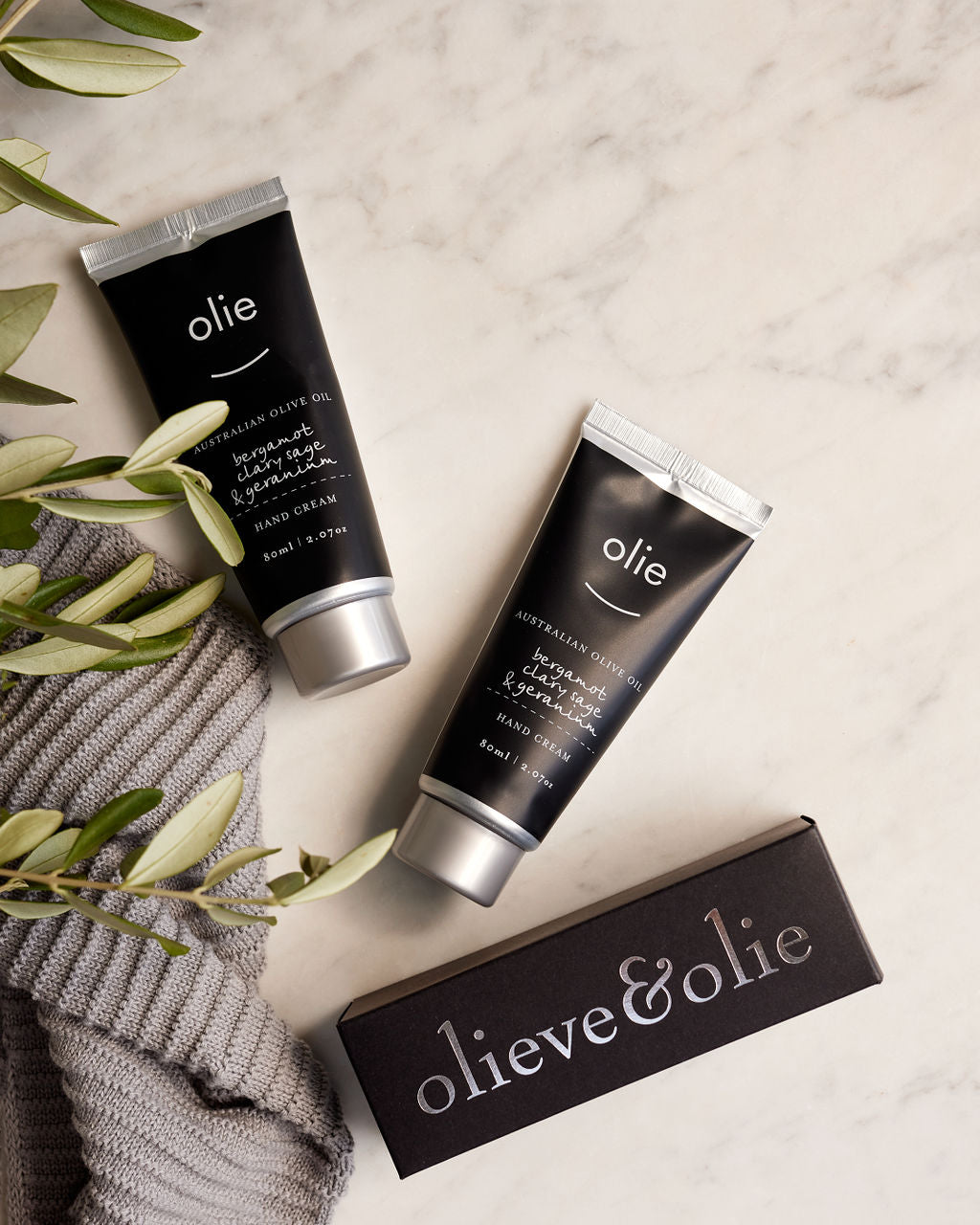 Olieve & Olie Bergamot, Clary Sage & Geranium Hand Cream arranged in a flat lay on a marble surface. Handcrafted with Australian olive oil, cocoa butter and beeswax, this nourishing hand cream deeply hydrates and softens dry hands while leaving a subtle botanical fragrance