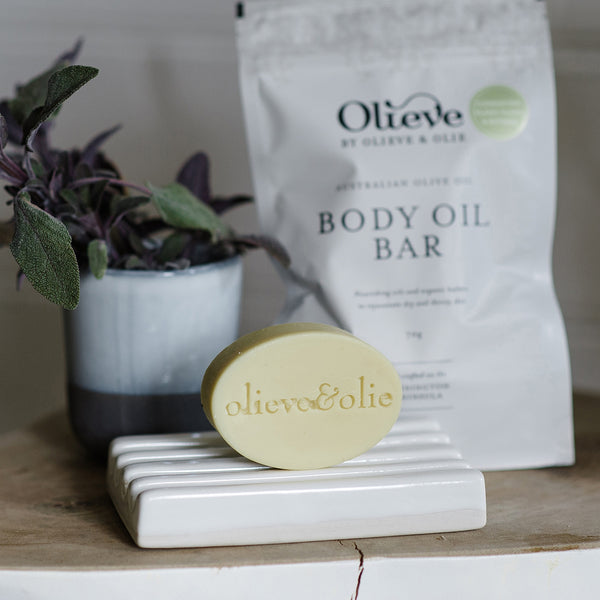 Olieve & Olie Clementine, Ylang Ylang & Nutmeg Body Oil Bar displayed on a small tray with fresh sage leaves in the background. This handcrafted solid moisturiser is made with Australian olive oil, cocoa butter and beeswax to deeply nourish, soften and protect the skin