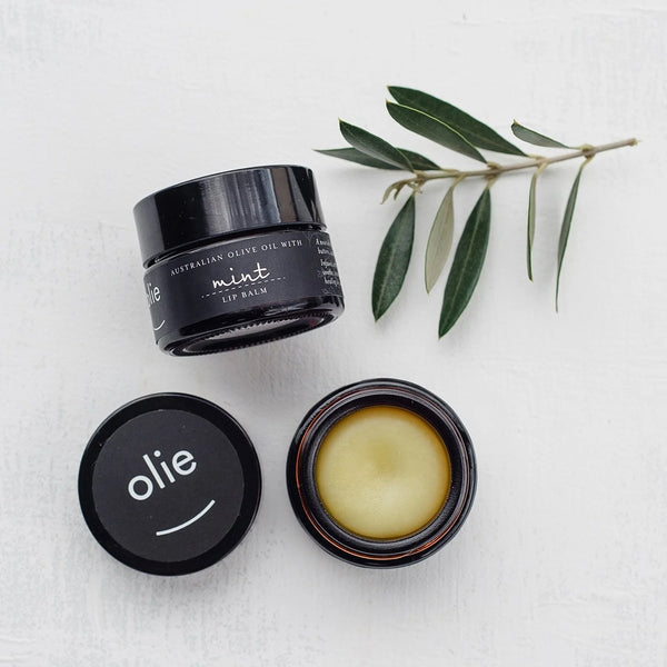 Olieve & Olie Mint Lip Balm displayed on a white background with a fresh olive leaf. Made with nourishing natural ingredients including Australian olive oil and beeswax, it helps keep lips soft, smooth and hydrated