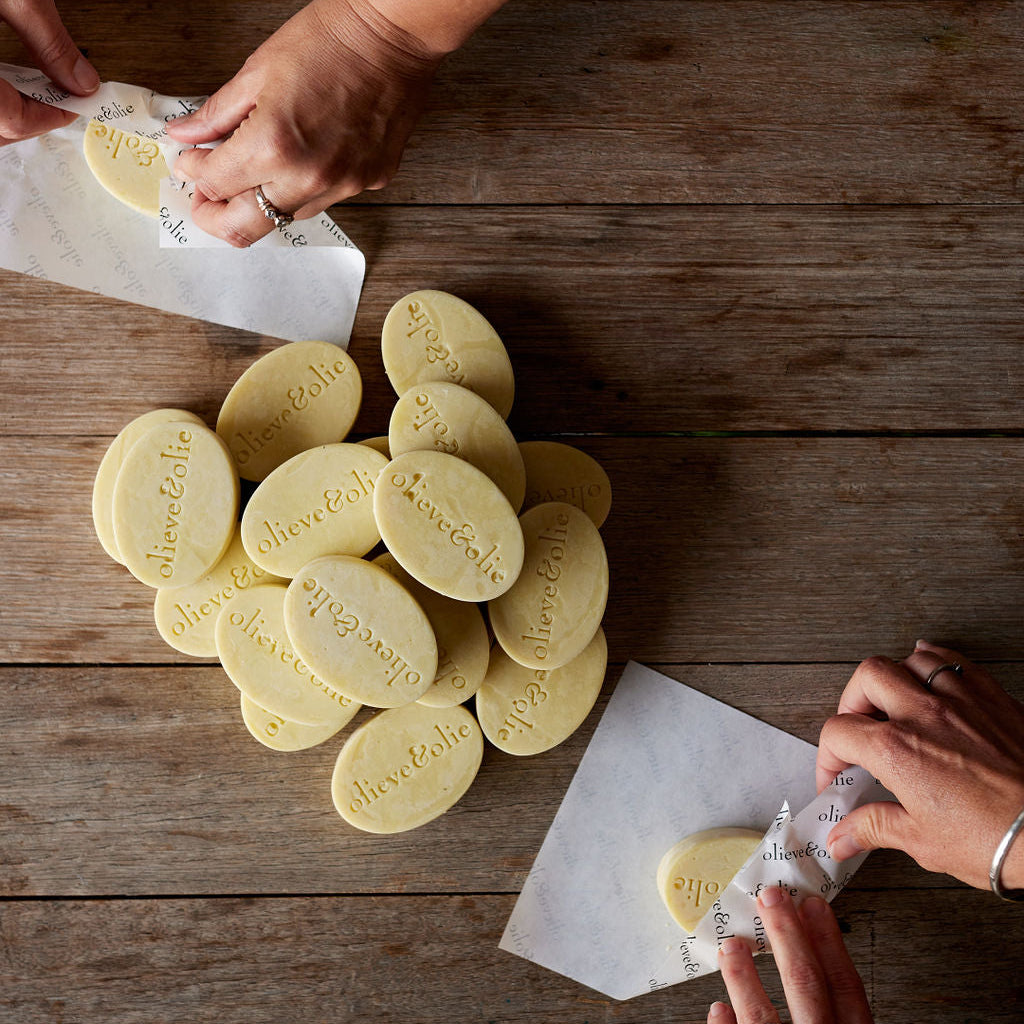 Hands wrapping handmade olive oil body oil bars on a wooden workbench on the Mornington Peninsula