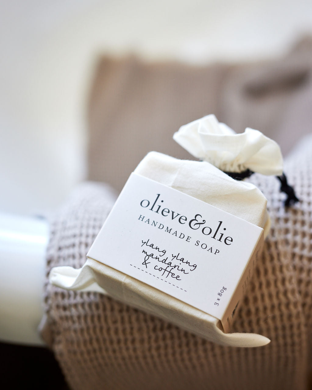 Olieve & Olie Ylang Ylang, Mandarin & Coffee Handmade Bar Soap displayed on the edge of a bathtub beside a soft waffle towel. Handcrafted with Australian olive oil using the traditional cold process method, it gently cleanses while helping maintain the skin's natural moisture balance