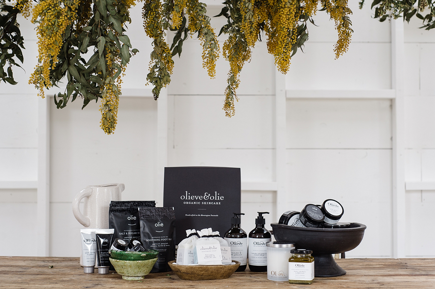 Olieve & Olie's range of skincare products on a table with florals hanging from the ceiling.