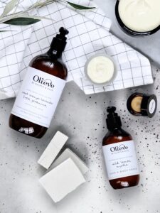 Olieve & Olie skincare products as a flat lay on a flat surface with olive leaves and a table cloth in black and white 
