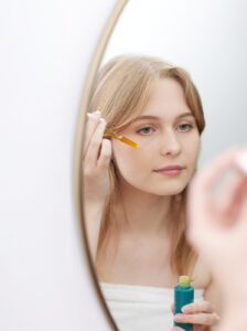 Girl uses face oil in mirror.